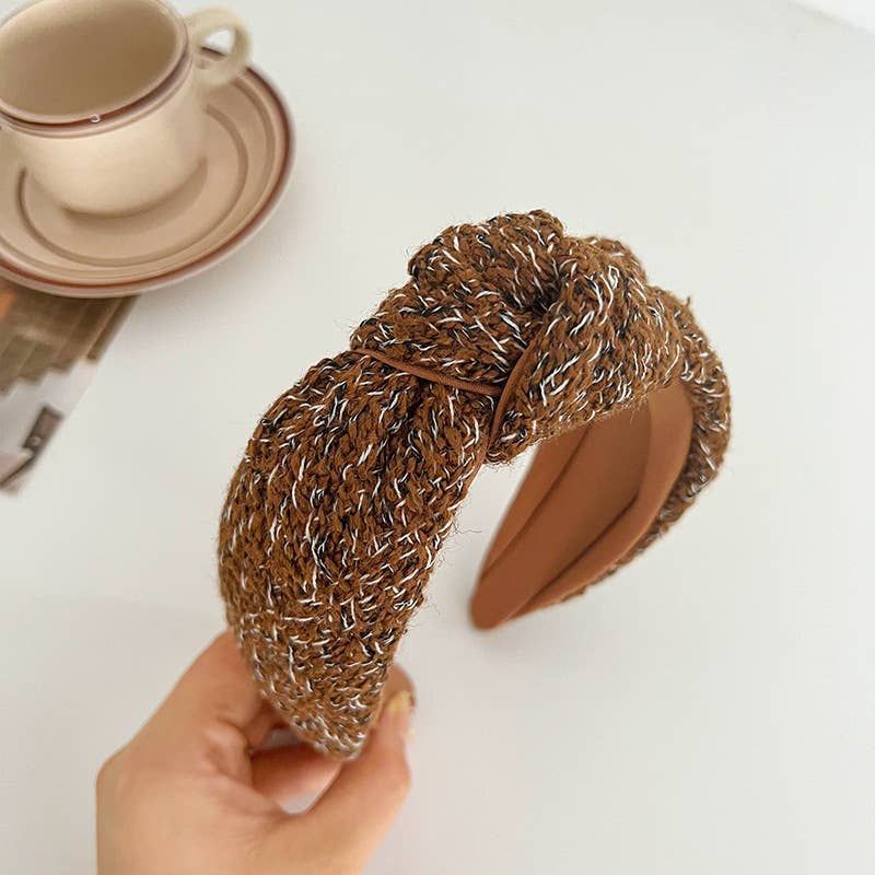 Brown and white textured knot headband held in a hand near a coffee cup.