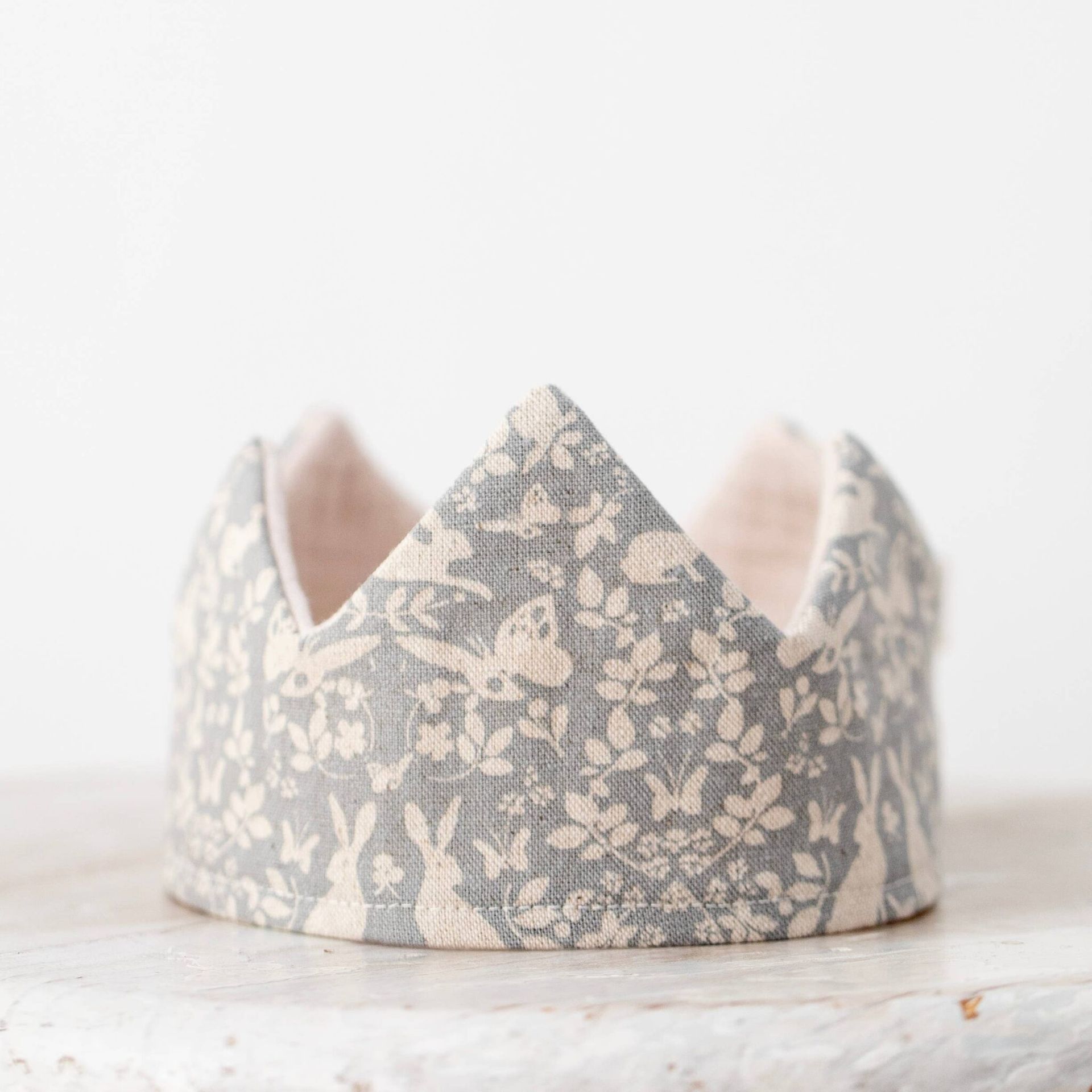 Fabric crown with a gray and white forest pattern, sitting on a surface.