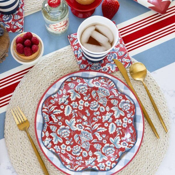 Table setting with floral plate, gold cutlery, and cold beverage; red, blue, and white colors.
