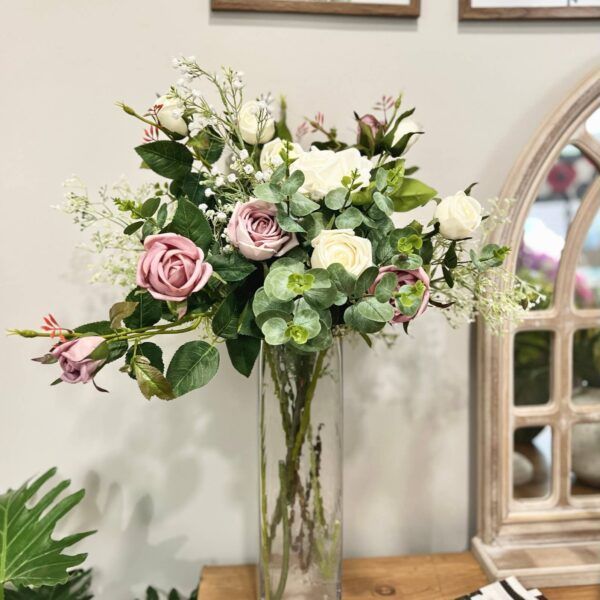 Bouquet of roses and greenery in a tall glass vase on a wooden surface.