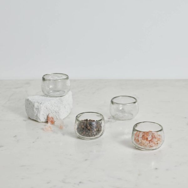 Small glass bowls holding salt and pepper, arranged on a white surface with a stone.