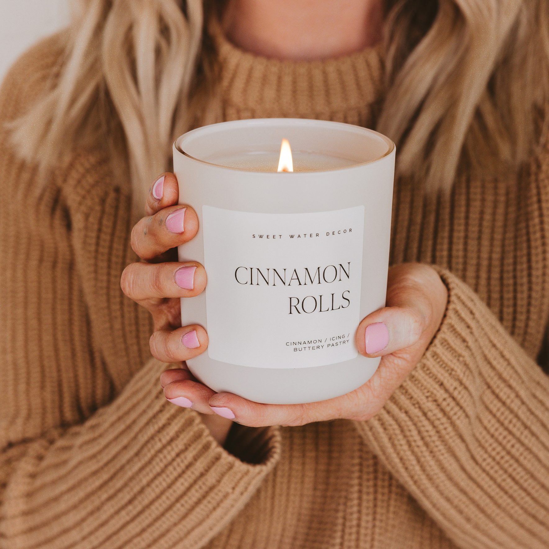 Woman holding a lit cinnamon rolls scented candle.