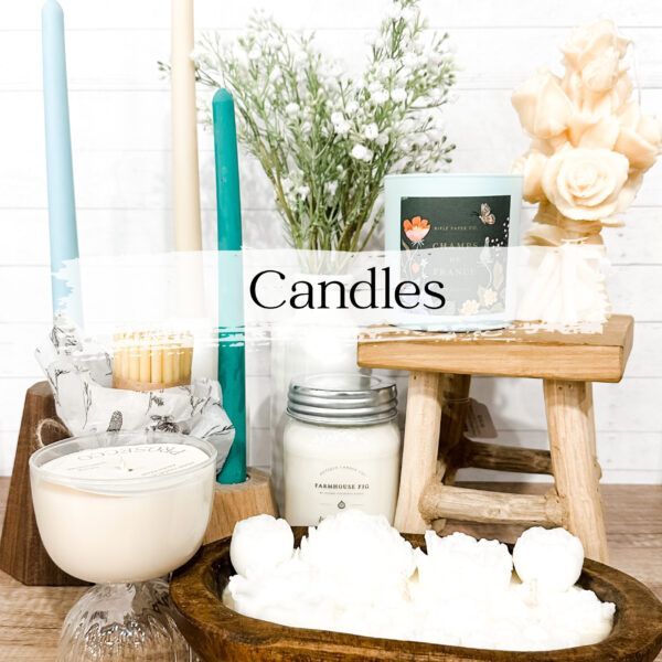 Various candles in different shapes and colors, arranged on a table with flowers.