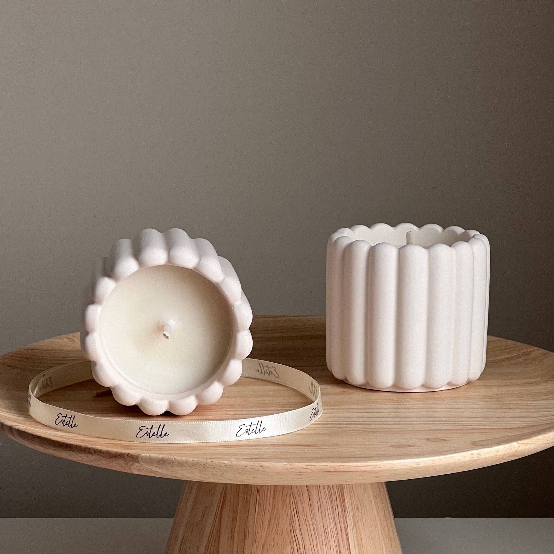 Two pink scalloped candles on a wooden stand. One is lit, and one is empty.