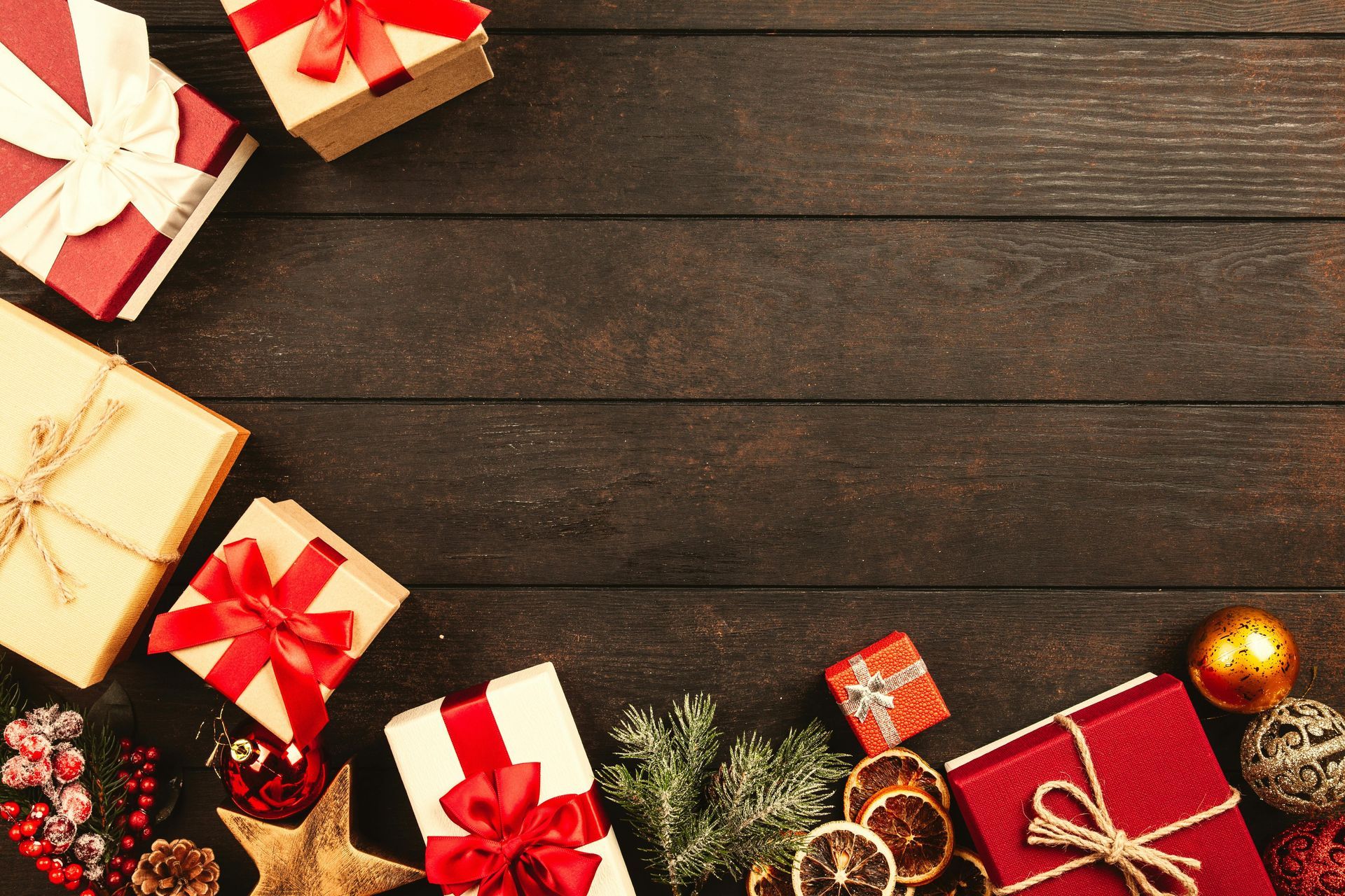 Gift boxes with red ribbons and Christmas decor on a dark wood surface.