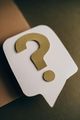 White speech bubble with a gold question mark on a brown background.
