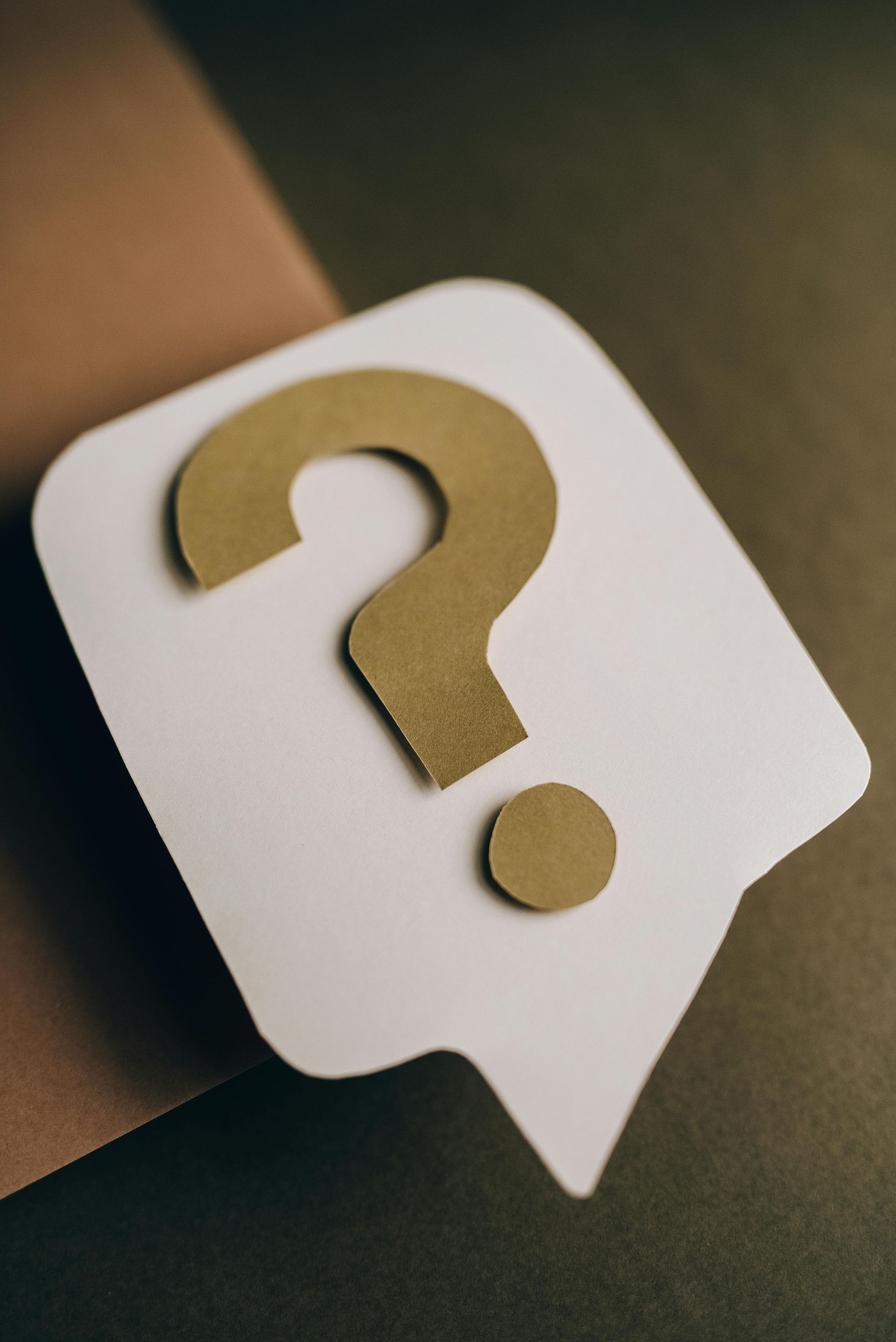 White speech bubble with a gold question mark on a brown background.