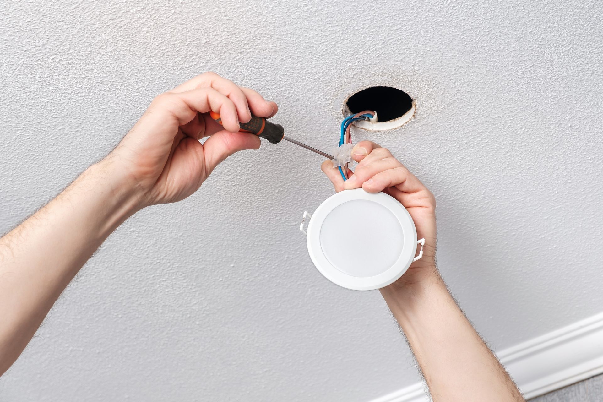 Person installing a ceiling light fixture with a screwdriver near exposed wires.