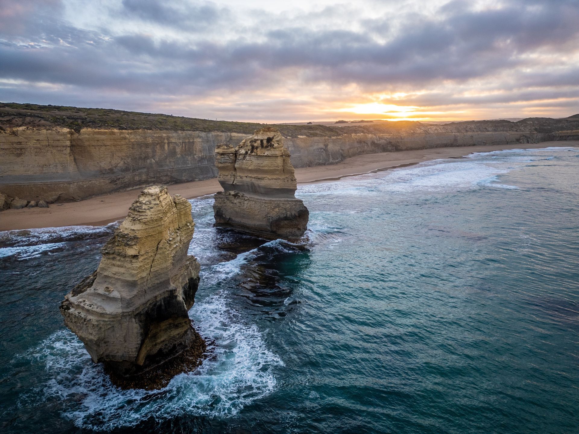 Two weathered rock formations rise from turquoise ocean, beneath a cloudy sunset.