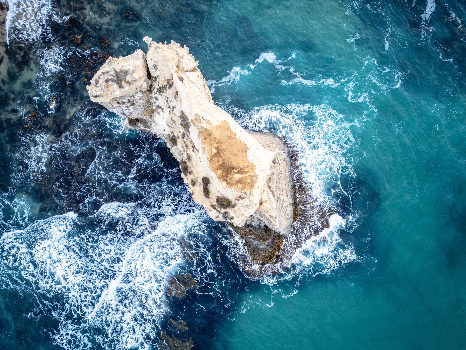 Rock formation in turquoise ocean; waves crashing around the stone.