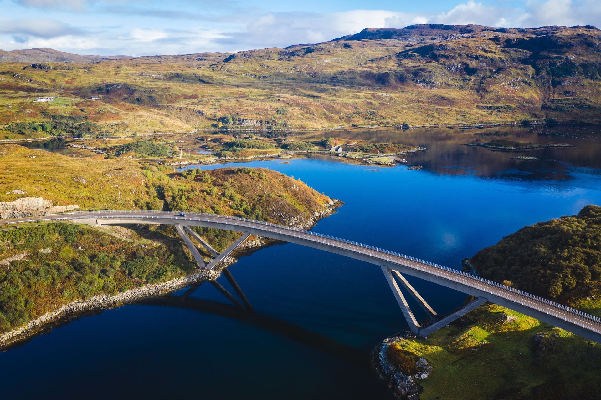 A curved bridge spanning blue water in a hilly landscape.