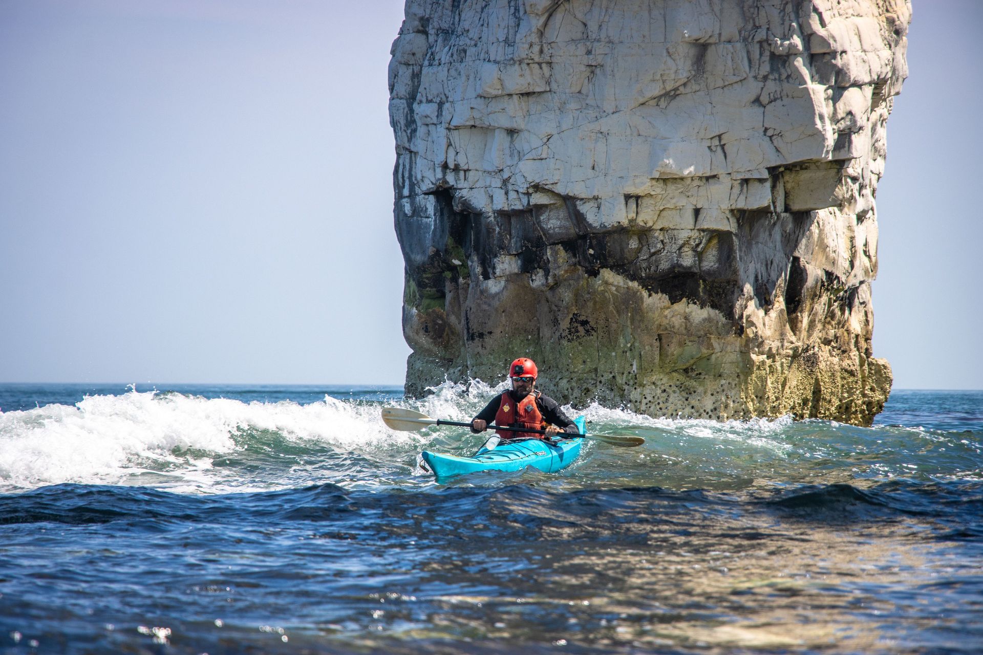Person kayaking in a blue kayak near a large, white rock formation in the sea.