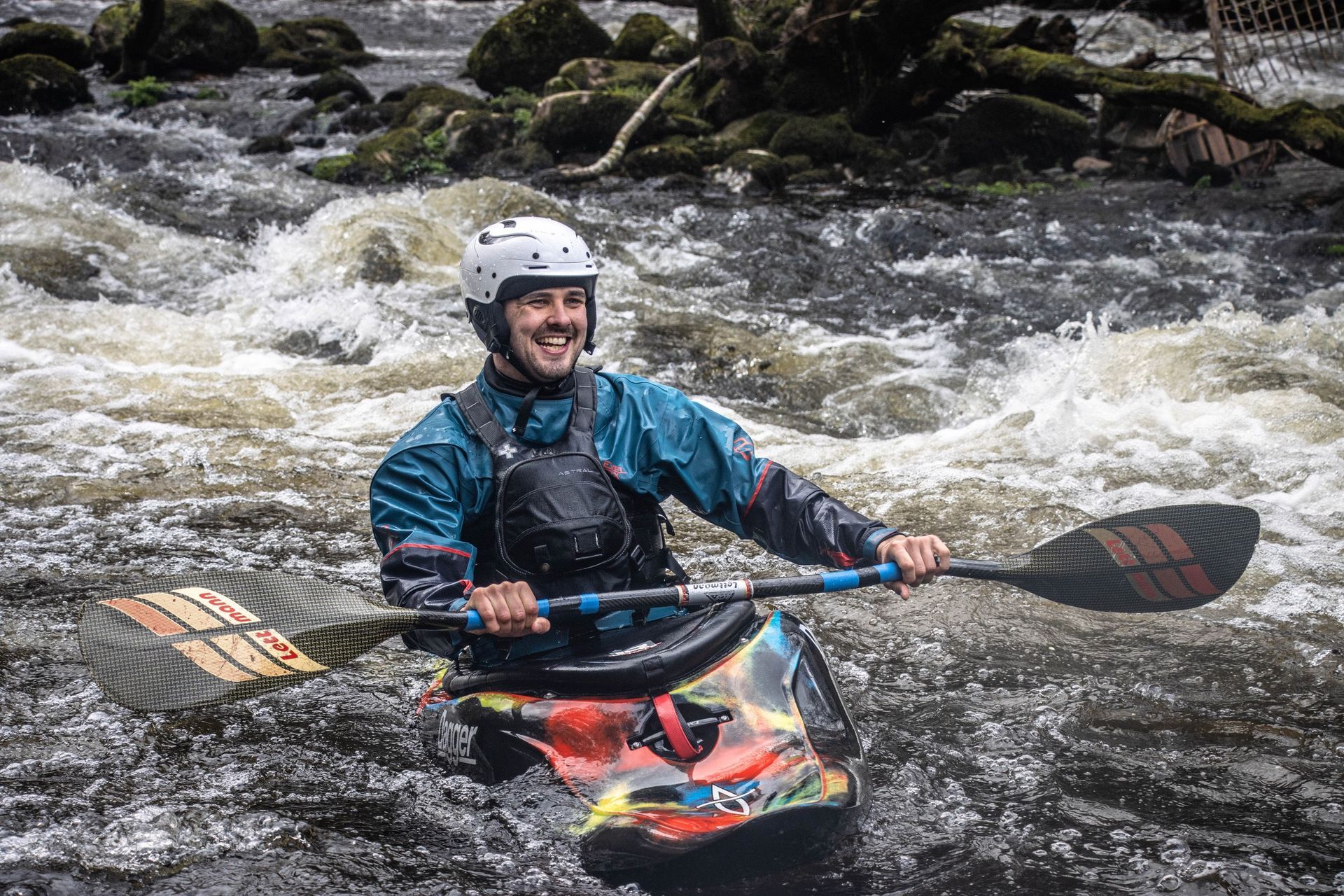 Kayaker in blue gear smiles while navigating white water rapids.
