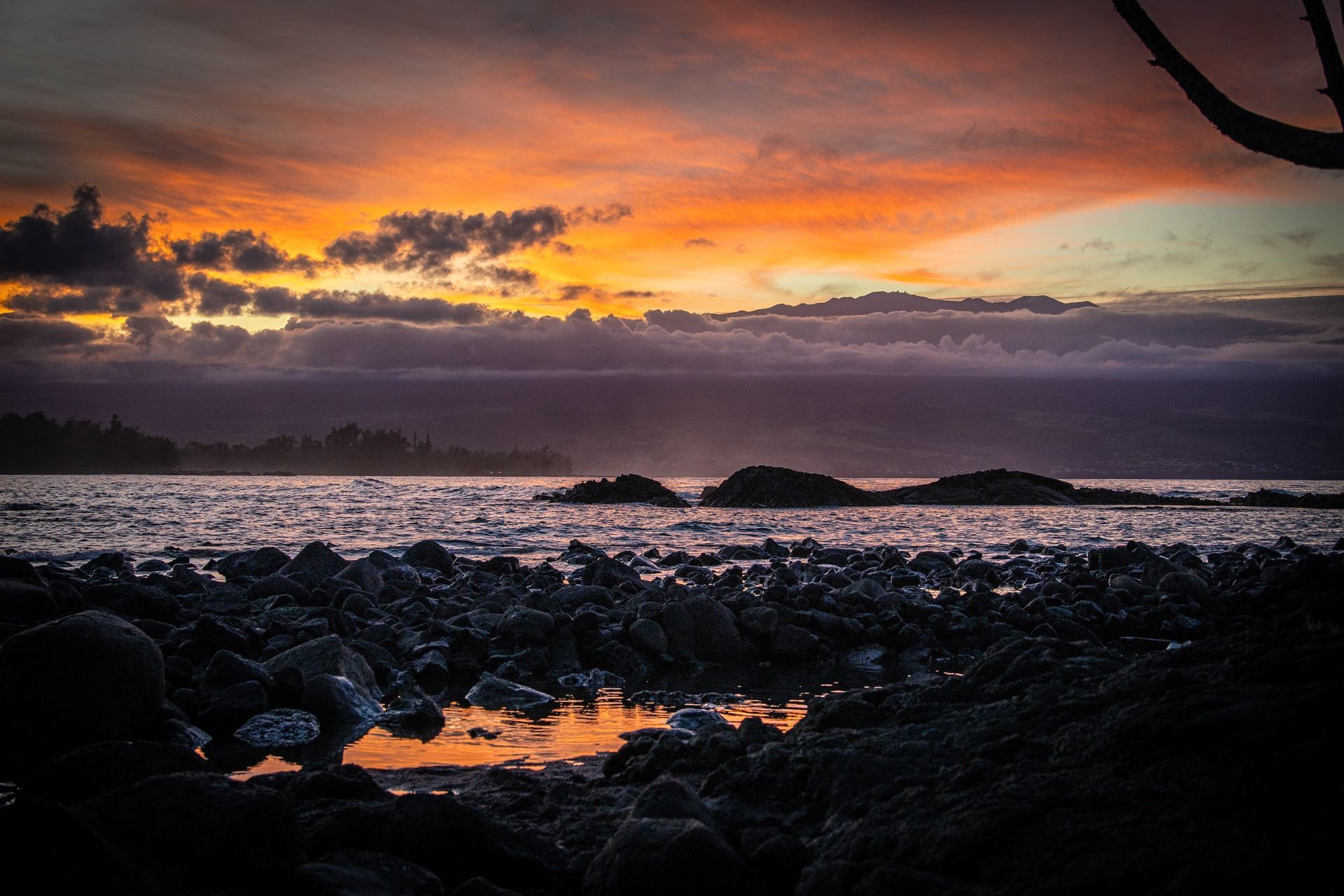 Sunset over ocean with orange and purple sky, rocky shoreline.