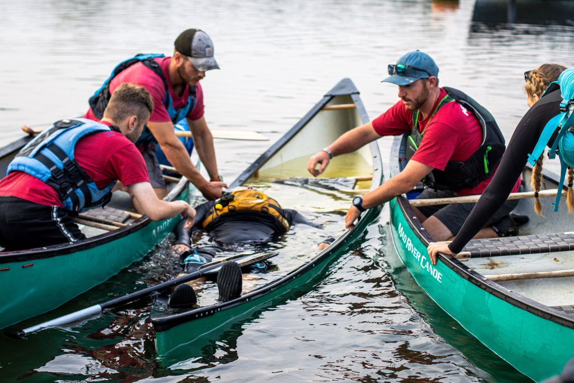 People in canoes, assisting someone who is submerged, possibly after a capsize, in a body of water.