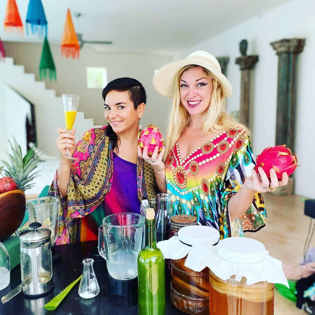 Two women are sitting at a table holding fruit and drinks.