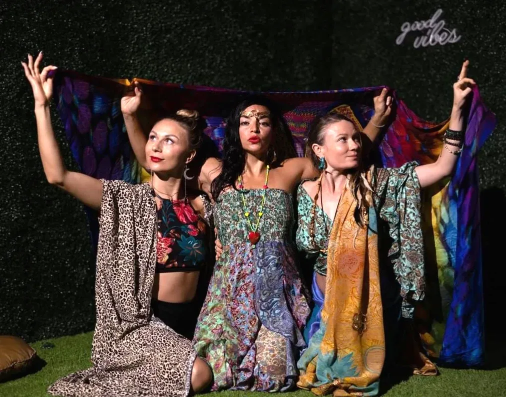 Three women are posing for a picture in front of a sign that says good vibes