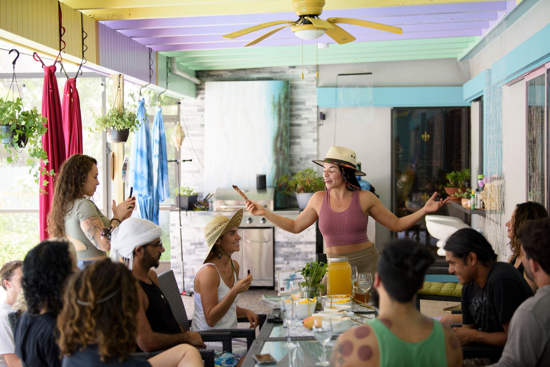 A group of people are sitting around a table with a woman standing in the middle of the room.