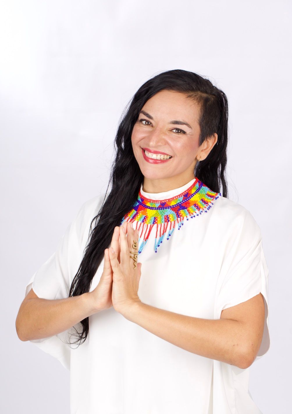 A woman wearing a white shirt and a colorful necklace is smiling.
