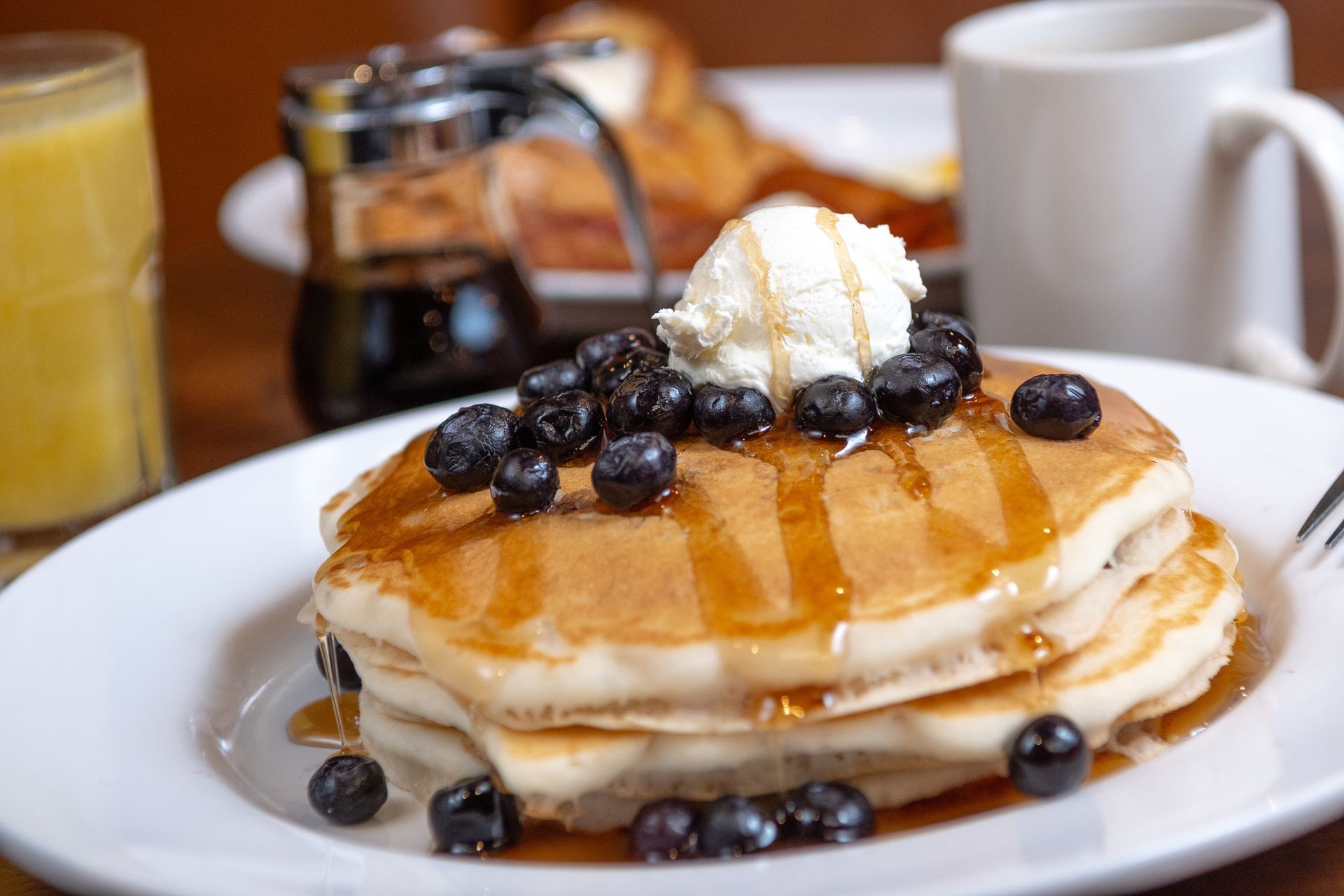 Stack of pancakes with blueberries, syrup, and whipped cream on a white plate, breakfast.