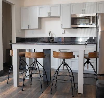 Kitchen with gray cabinets, a stainless steel microwave, and a breakfast bar with three stools.