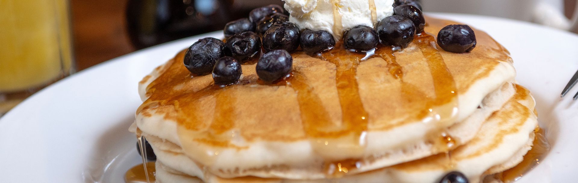 Stack of pancakes with blueberries, syrup, and whipped cream on a white plate.