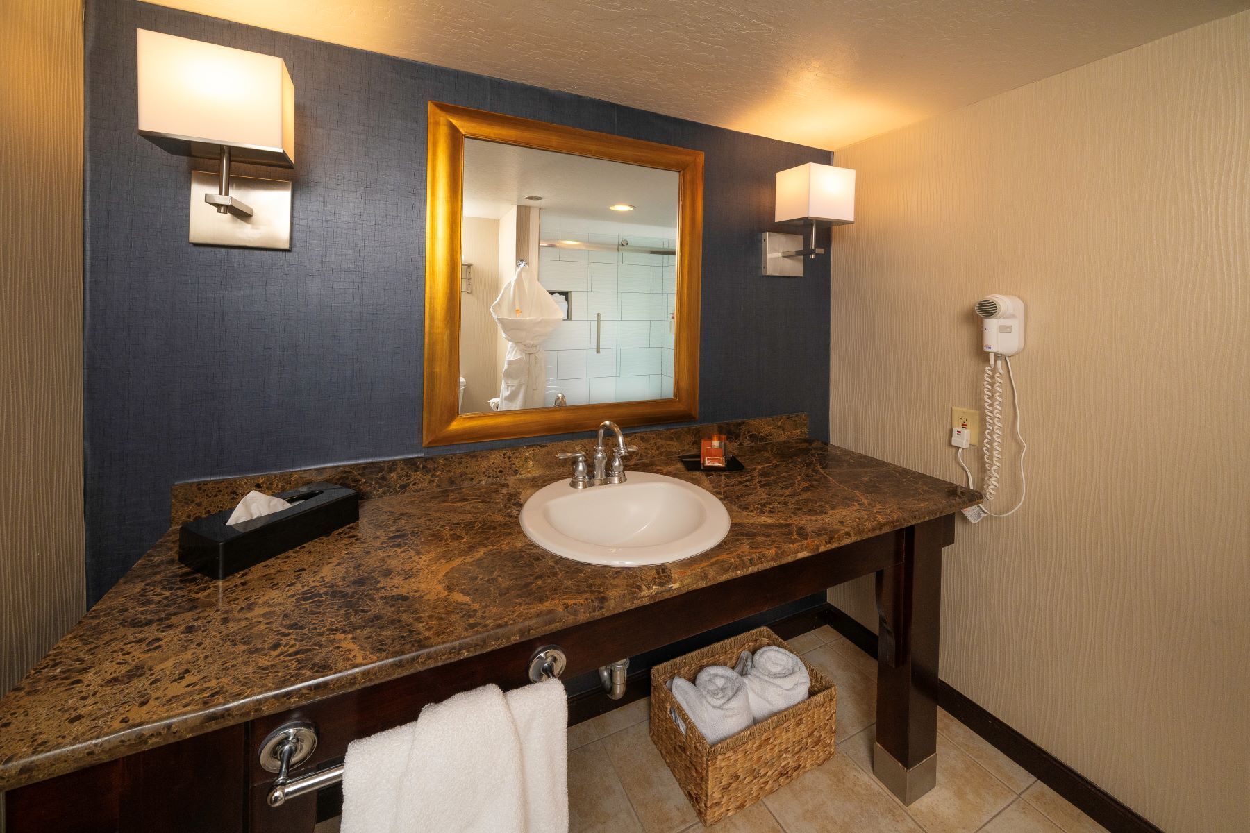 Bathroom with marble countertop, sink, mirror, and two wall sconces. Includes towels and hairdryer.