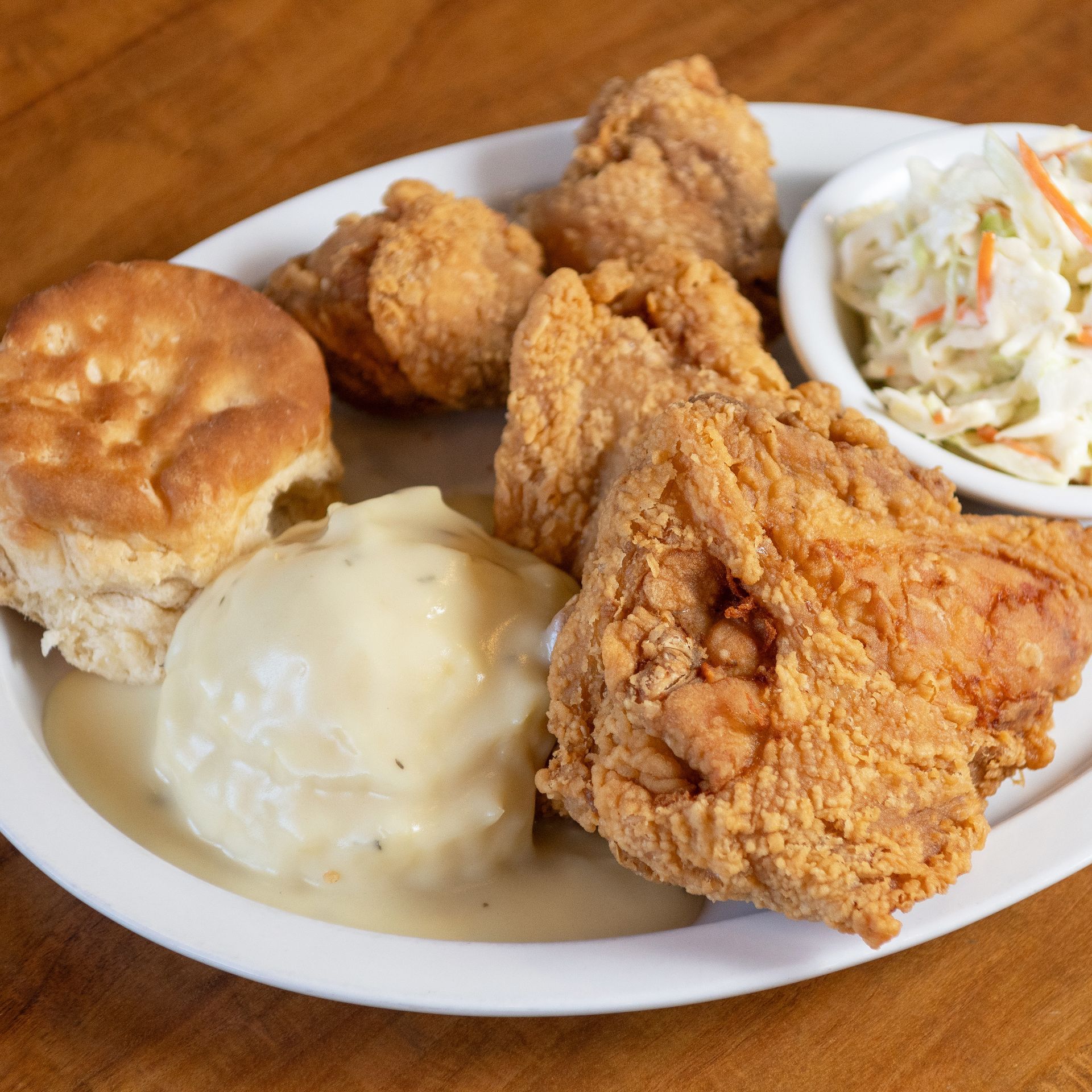 Plate of fried chicken, mashed potatoes with gravy, biscuit, and coleslaw.