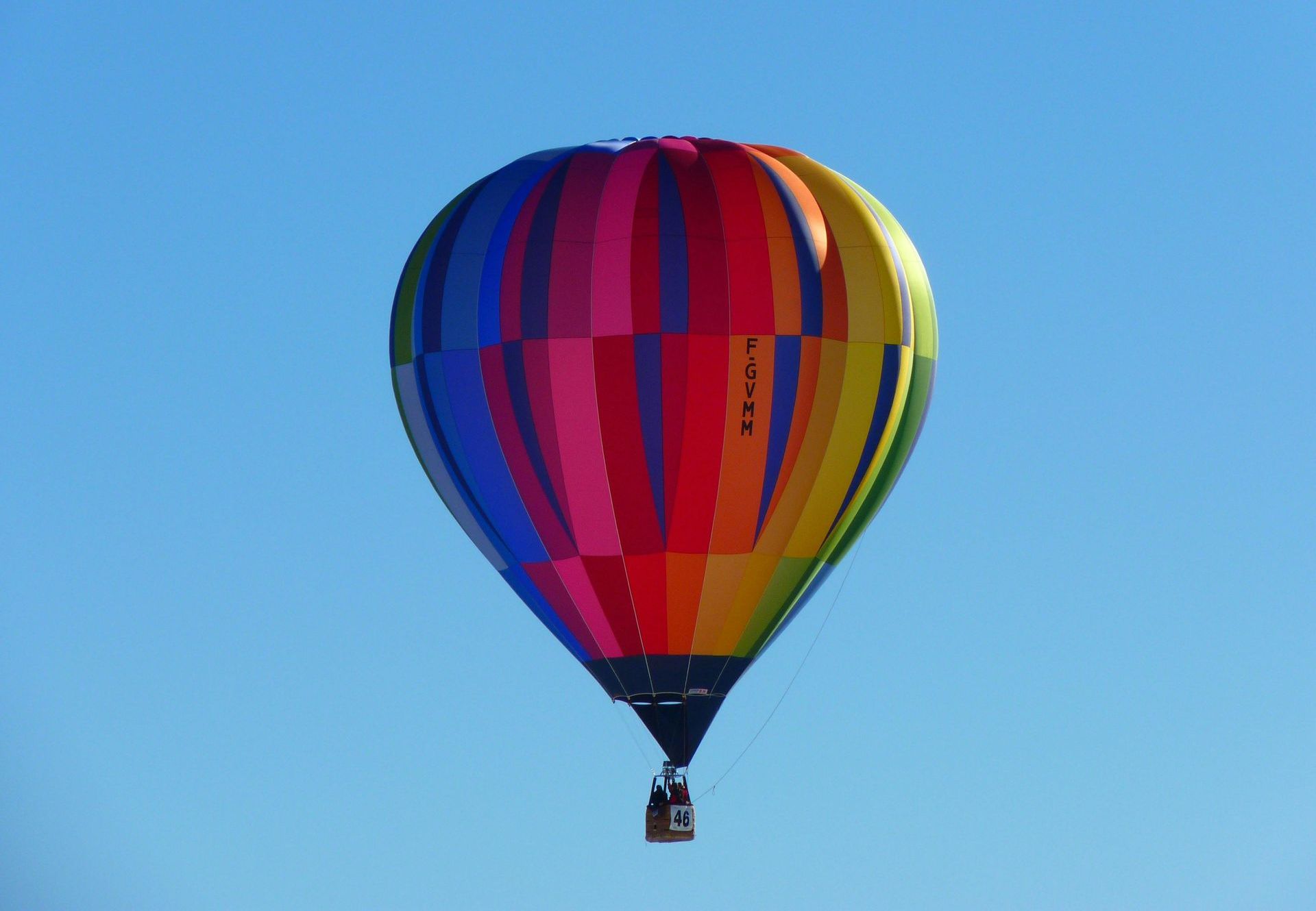 Colorful hot air balloon soaring in a clear blue sky.