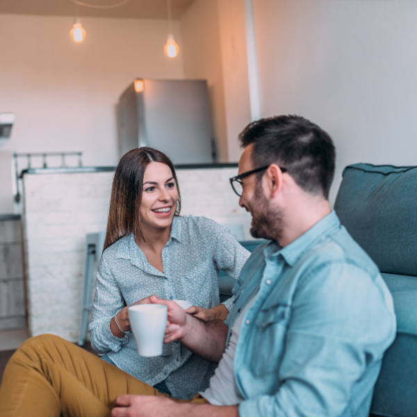 a man and a woman are sitting on a couch drinking coffee .