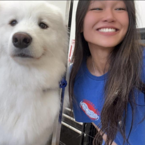 Woman smiling beside a fluffy white dog, both close to the camera indoors