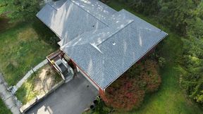 Overhead view of a house with a gray roof, surrounded by green grass and some reddish bushes.