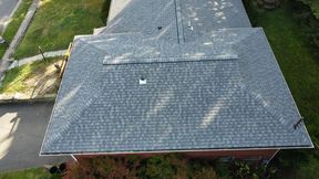 Overhead view of a house with a gray shingled roof, set in a neighborhood with a street and trees.