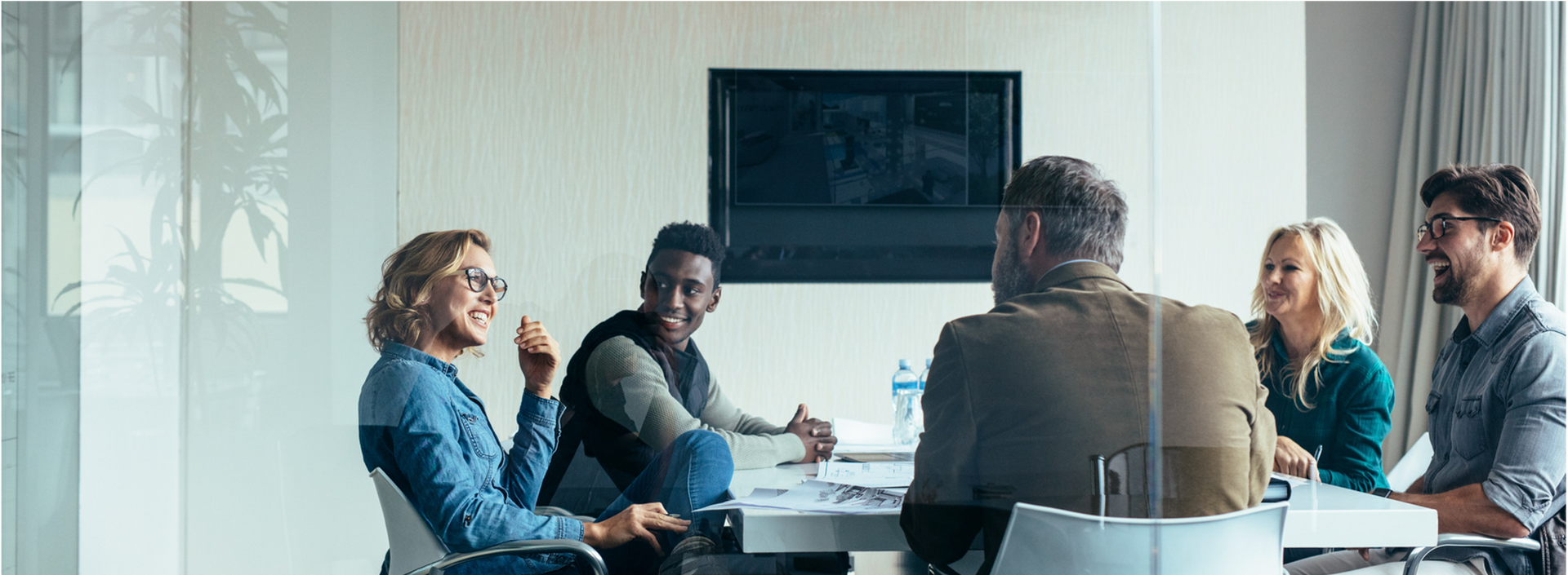 People in a bright meeting room sit around a table in a team discussion.