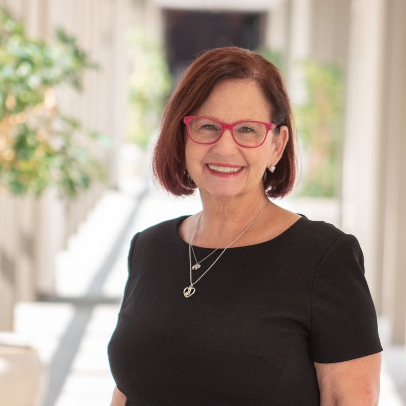Smiling woman with red glasses and short auburn hair in a bright hallway