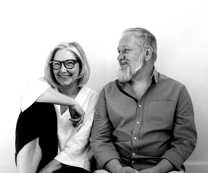 Two smiling people seated together, one leaning toward the other in a casual black-and-white portrait.