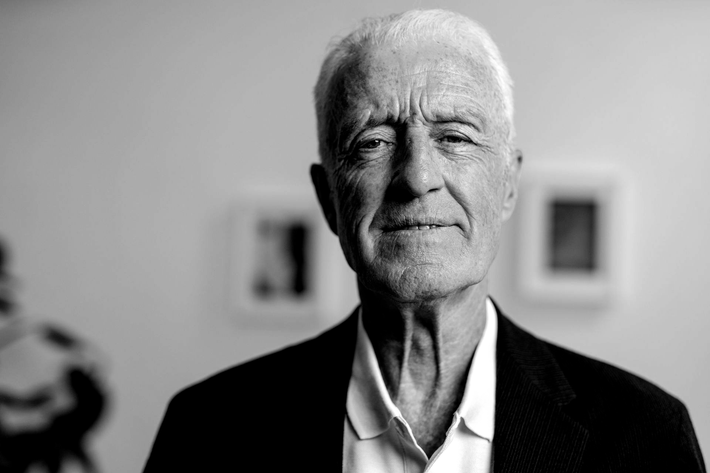Black-and-white portrait of an older man in a blazer, facing forward with a slight smile.