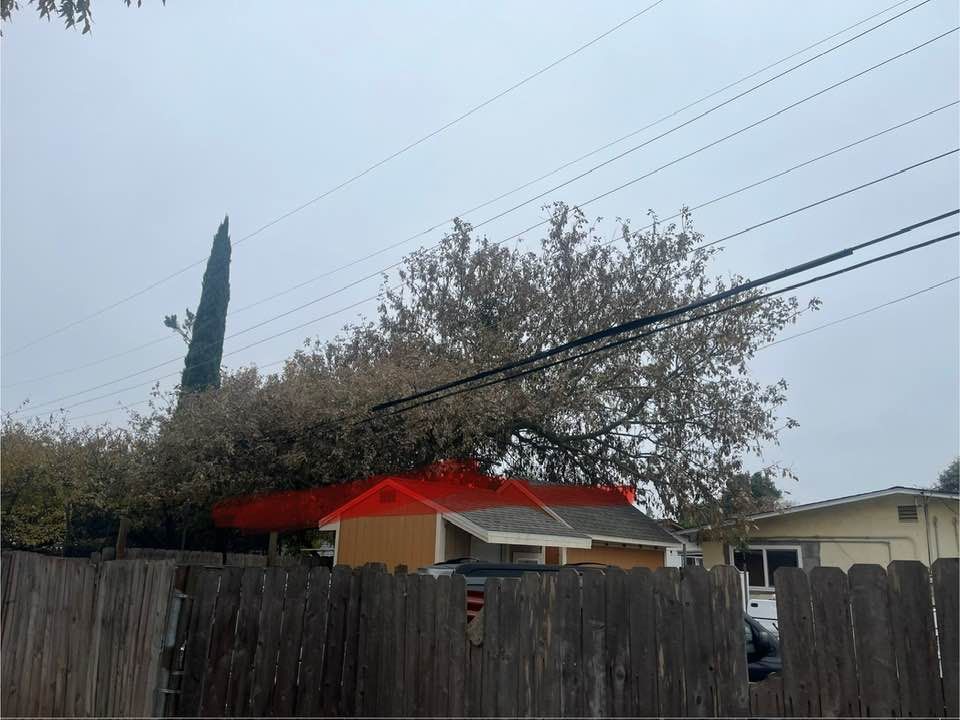 Wooden fence in front of a house with a red roof, trees, and power lines against a cloudy sky.