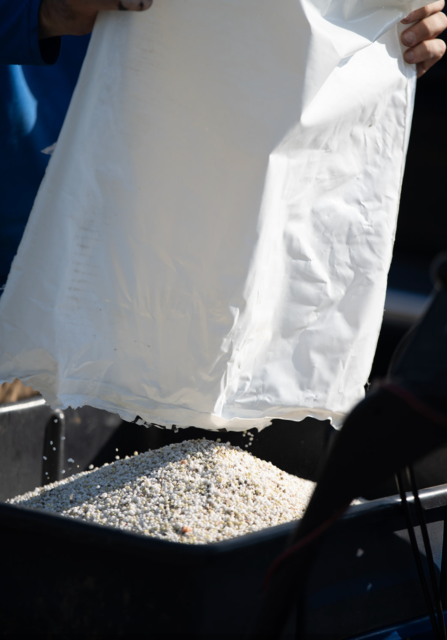 Person holding open white bag over a container of small pebbles outdoors