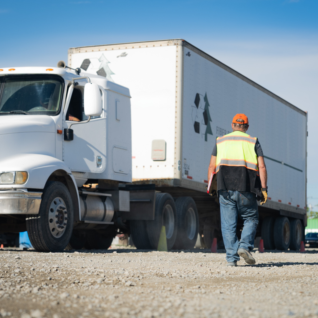 cdl student walking in training yard wearing a vest with a semi truck in the backgound.