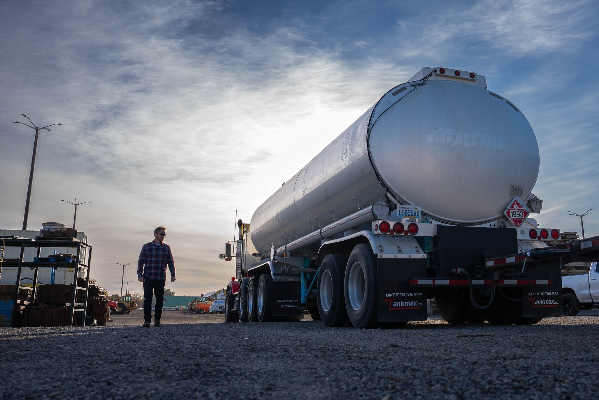 Fuel tanker truck parked on gravel at dusk, with a person walking nearby under a cloudy sky