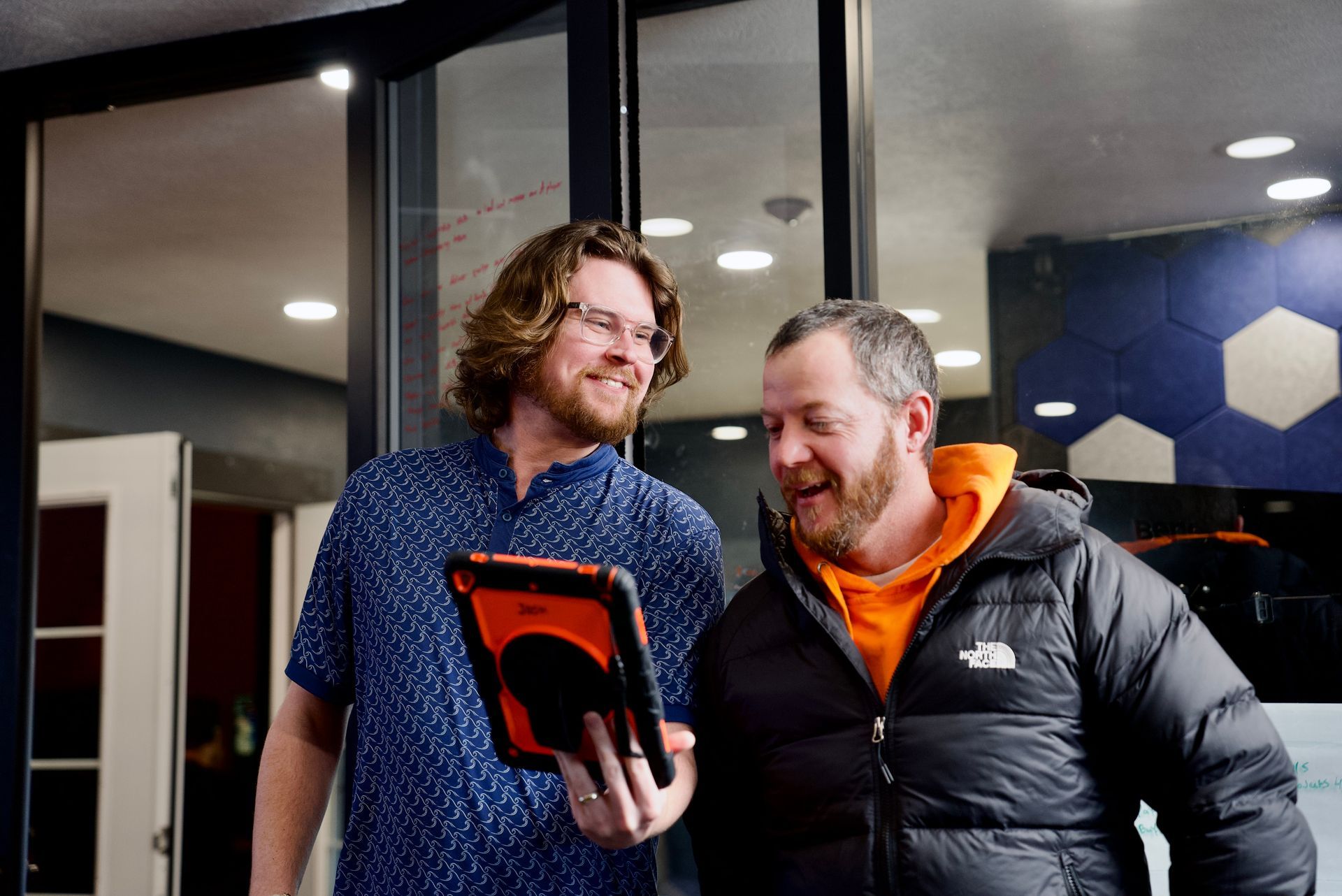 Two people smiling and looking at a tablet in a modern office lobby