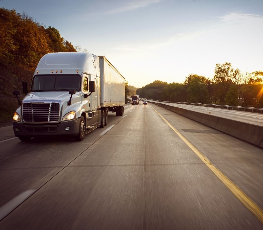 A semi truck is driving down a highway at sunset.