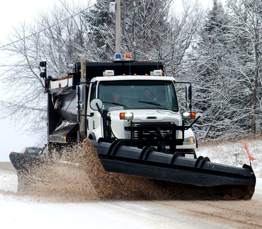 A snow plow is driving down a snowy road