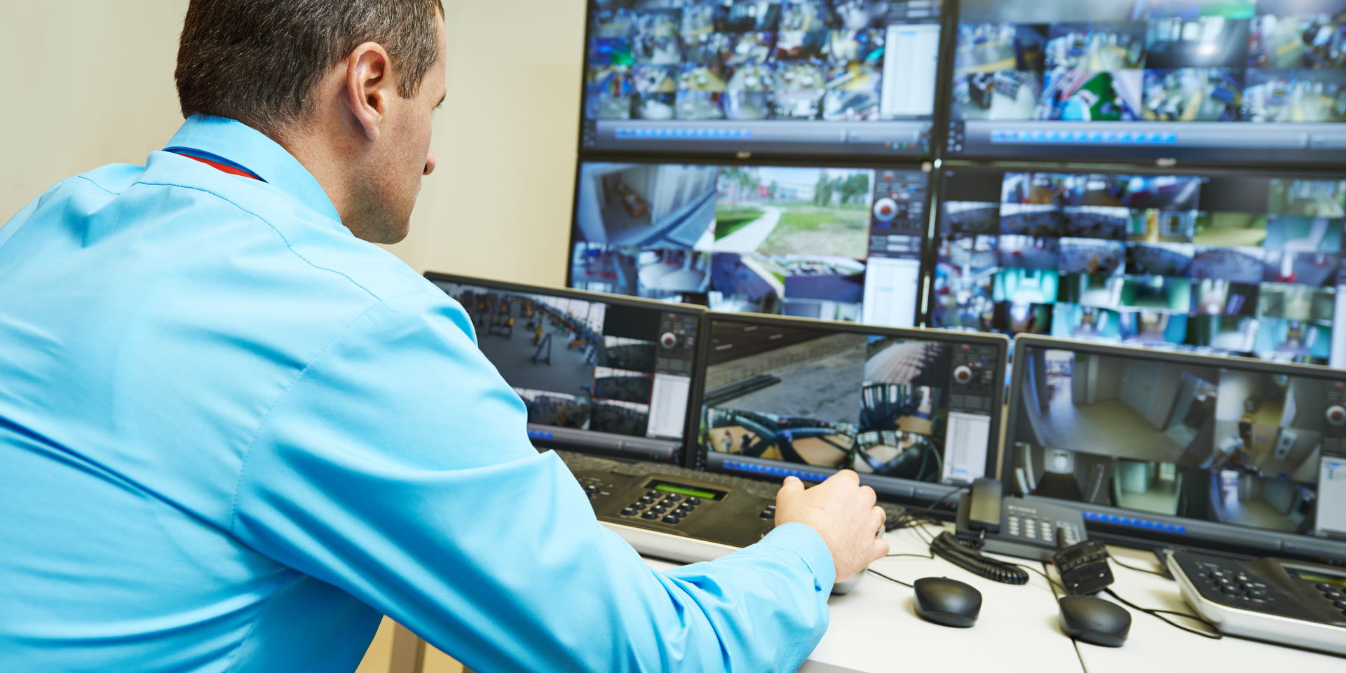 A1 Security Guard a man in a blue shirt sits at a desk looking at security monitors