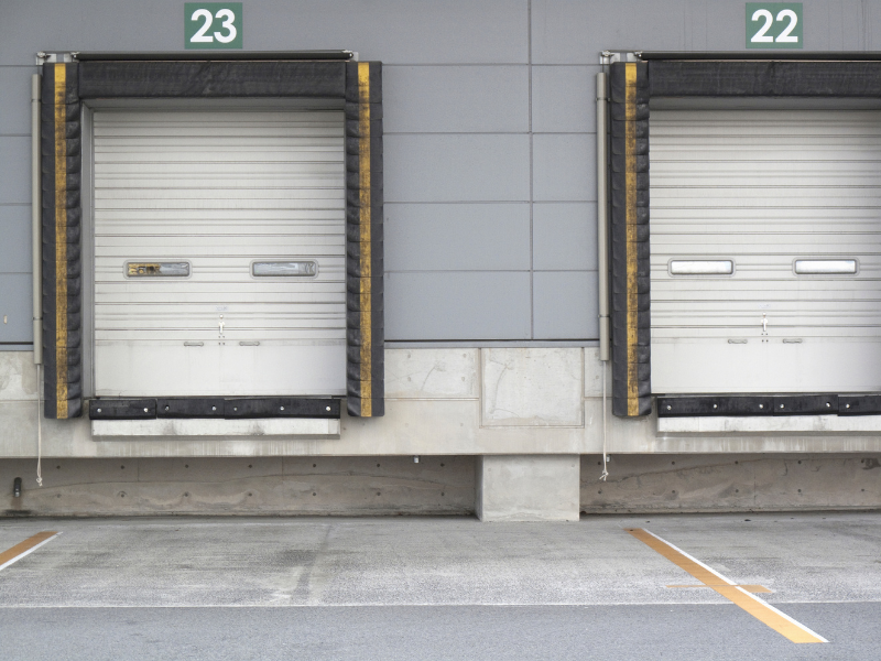 Loading dock with two closed white roll-up doors labeled 23 and 22 on a gray building