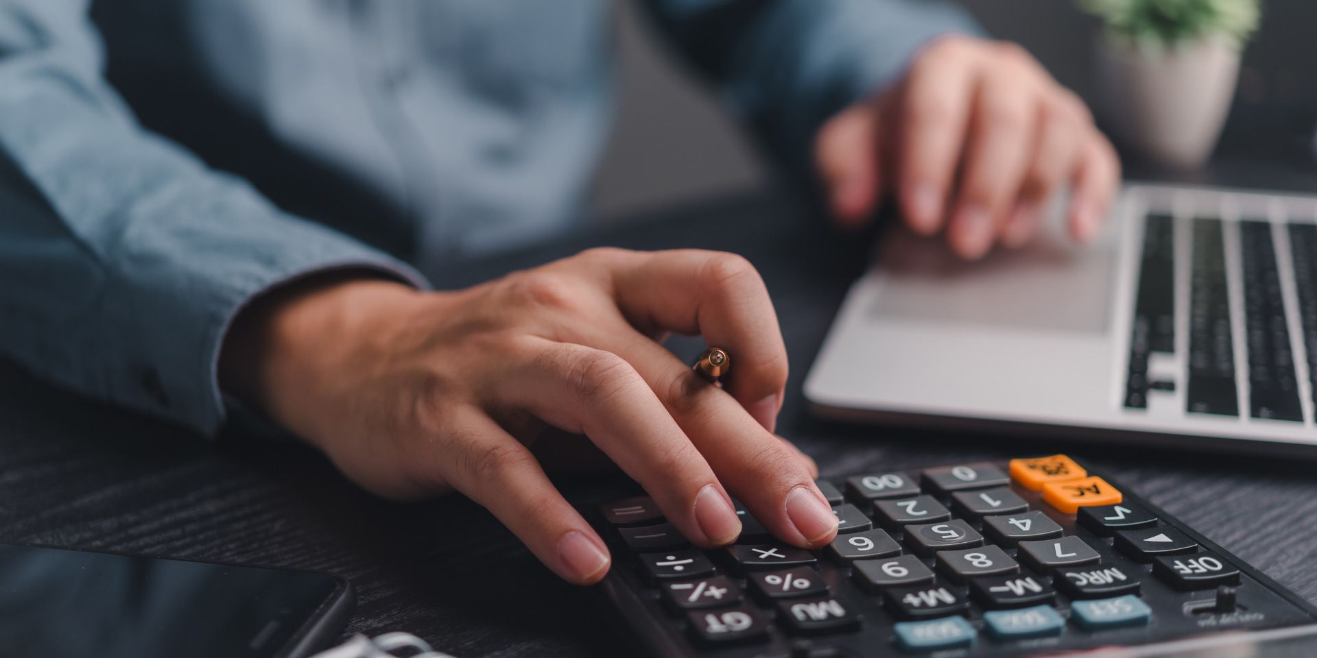 Hand using a calculator beside a laptop on a desk