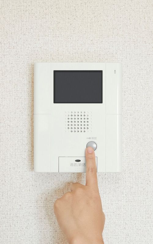 Hand pressing a wall intercom with screen and speaker grille