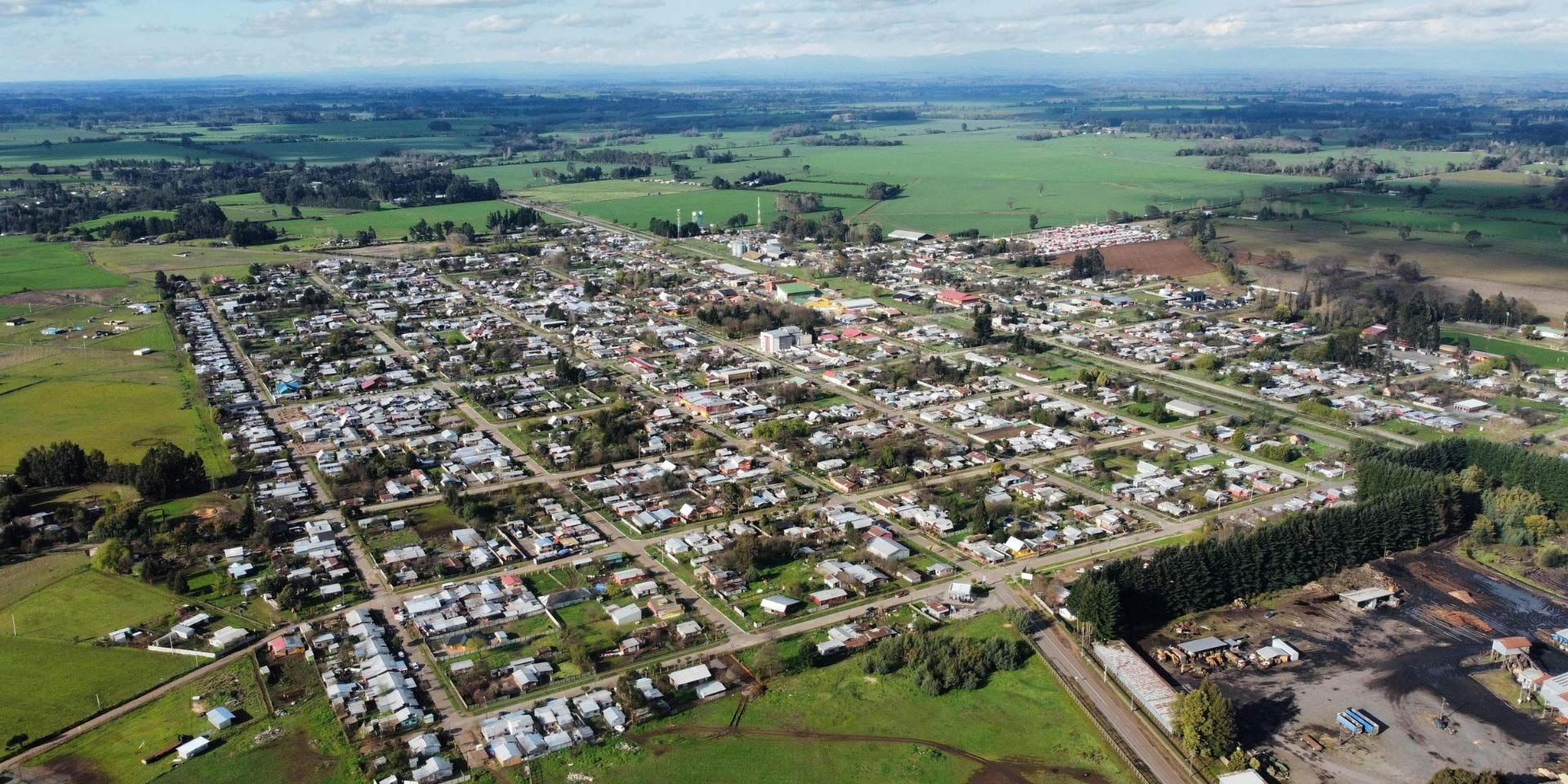 Aerial view of a small town surrounded by green fields and farmland under a hazy sky