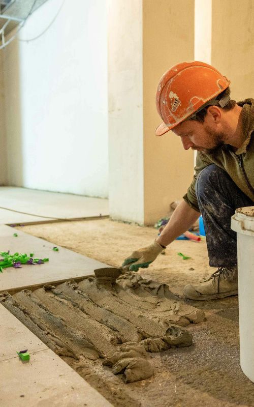 Construction worker in orange hard hat smoothing wet mortar on a floor repair site